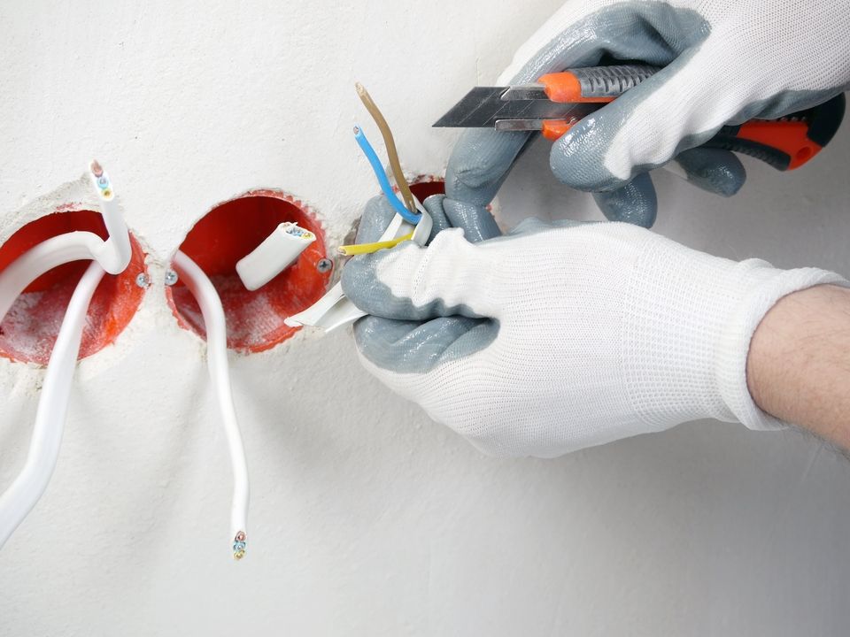 Nahaufnahme einer Hand mit weisen Handschuhen bei der Elektroinstallation